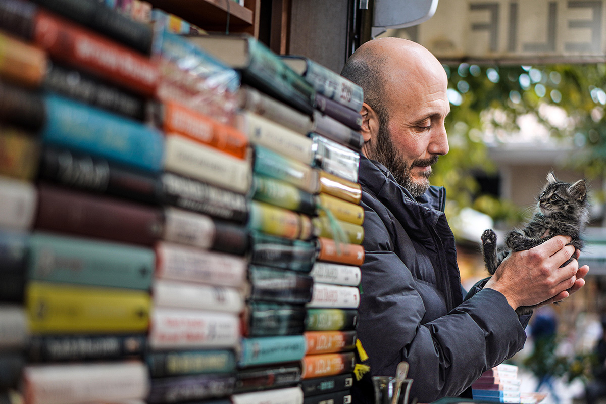 Man cradling a kitten beside a book stall in Istanbul