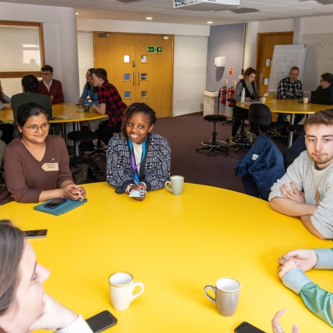 A group of students and staff seated around a table in a workshop session.