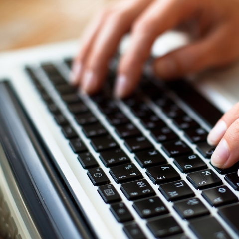 Close-up of hands typing on a laptop keyboard.