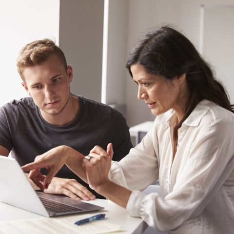 A student and a member of staff looking at a laptop together.