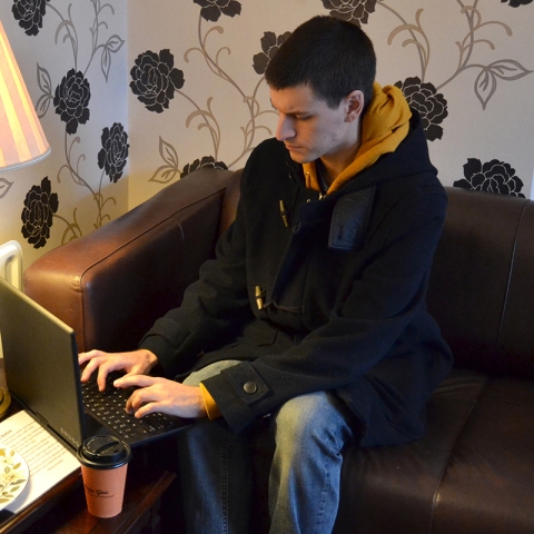 Male student chatting online in a cafe using a laptop