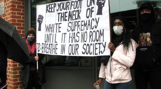 Black women protesting, carrying a sign reading "Keep your foot on the neck of white supremacy until it has no room to breathe in our society." - From Wikimedia Commons - https://commons.wikimedia.org/wiki/File:%27Black_Lives_Matter%27_protest_in_Norwich_-_one_of_the_banners_-_geograph.org.uk_-_6501038.jpg