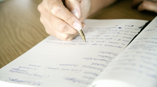 Close-up of a hand writing notes on paper with a pen.