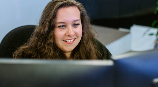 Woman - smiling, sat at a computer