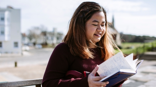 Headshot of female postgraduate smiling, reading a book outside
