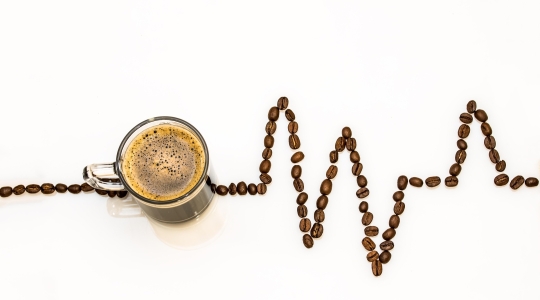 Coffee cup with coffee beans laid out in a line suggestive of an oscilloscope trace (heartbeat monitor)