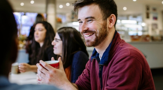 Students sat around a table smiling and talking in the Library Café