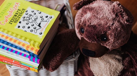 Teddy bear sat next to a pile of children's books written in an Eastern European language, from Pexels - https://www.pexels.com/photo/brown-bear-plush-toy-and-stack-of-books-4887203/
