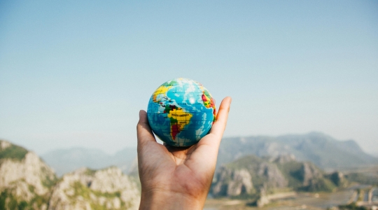 Hand holding up a small model globe of the world - from Pexels: https://www.pexels.com/photo/person-holding-world-globe-facing-mountain-346885/