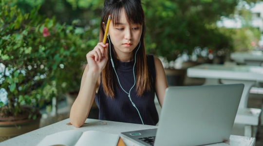 Asian woman sat outside with notebook and laptop