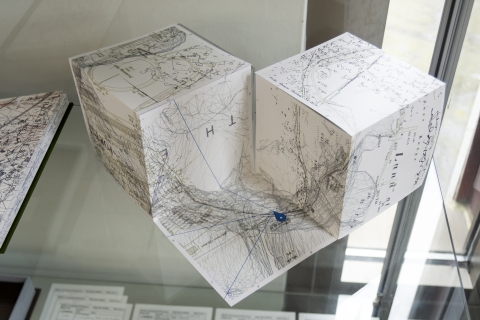Artist's book created from maps.  Two cubes formed from maps shelter a square map with a location marker 