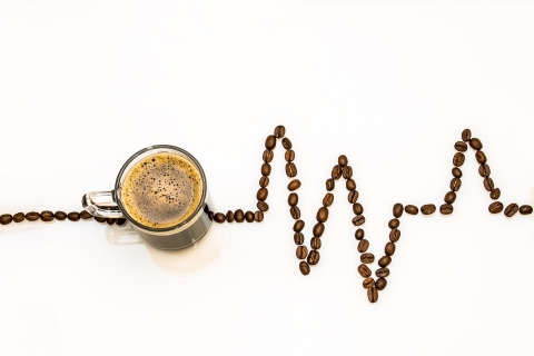 Coffee cup with coffee beans laid out in a line suggestive of an oscilloscope trace (heartbeat monitor)
