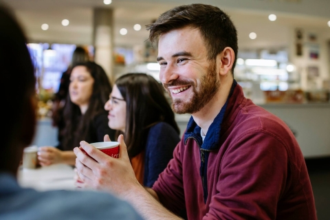 Students sat around a table smiling and talking in the Library Café