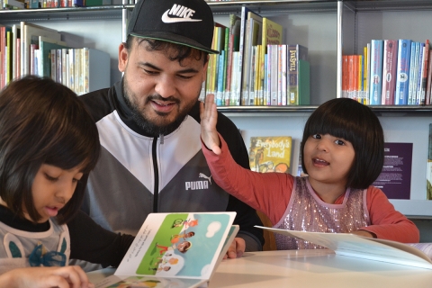 Father and children reading books from the Outside In World collection of global children's books in translation