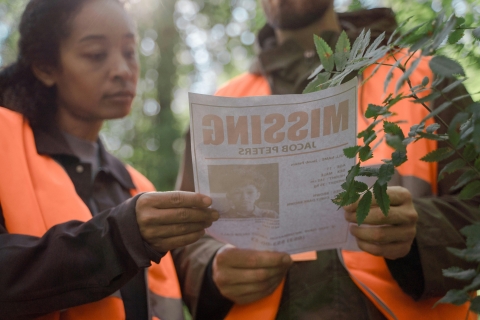 Two people in luminous jackets stood in a forest examine a poster for a missing individual