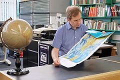 Photograph of Map Librarian in the Map Library. He is holding a map and standing next to a globe.