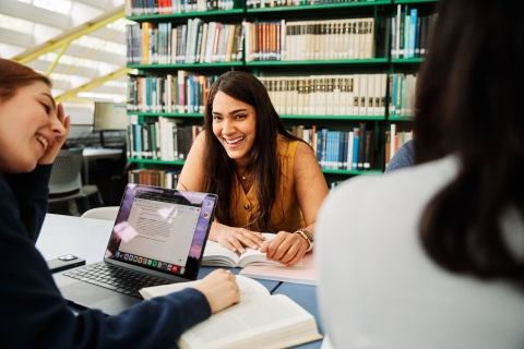 Young women studying and socialising in the Library with books and laptops