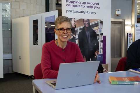 CCI Faculty Librarian Greta Friggens sat in the Library Atrium in front of the Library pop-up banner