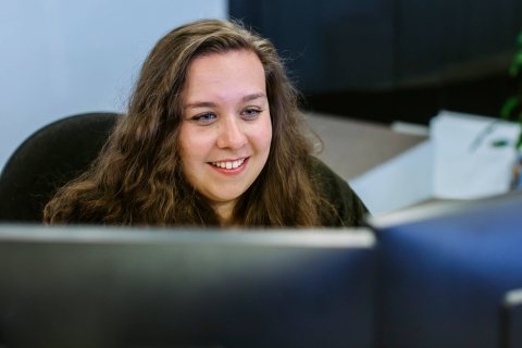 Woman - smiling, sat at a computer