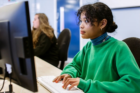 Student wearing green jumper sitting at a computer looking at the screen