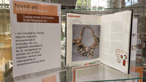 Open book displaying a photograph of a found art necklace next to a sign explaining the nature of found art.