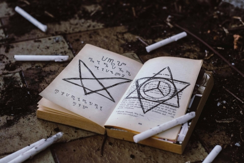 A ring of extinguished white wax candles surrounding an open book on which has been drawn arcane sigils and motifs - from Pexels, https://www.pexels.com/photo/opened-book-3050270/