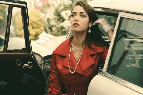 Woman in red coat and pearl necklace getting out of a vintage car, representing late 20th century womenswear.  From Pexels - https://www.pexels.com/photo/pretty-woman-posing-beside-a-vintage-car-8791108/
