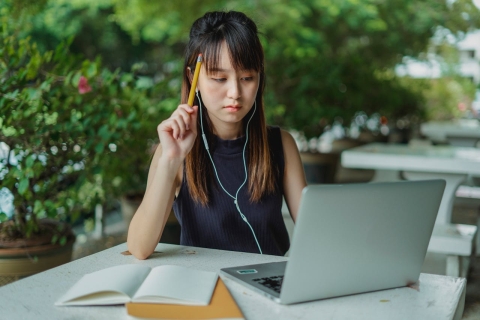 Asian woman sat outside with notebook and laptop