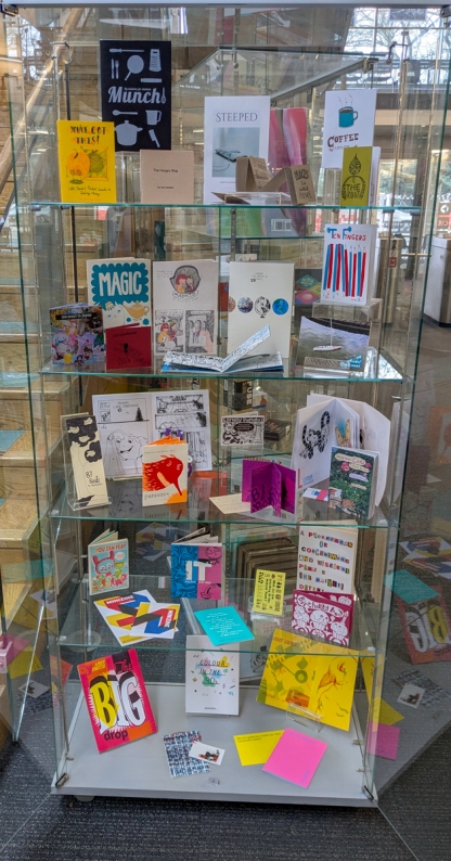 Glass cabinet displaying assorted zines produced by students and published zines available in the Library