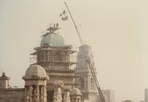 Galleon weathervane being lifted on a crane above the roof of Park Building
