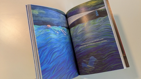 Open book depicting a girl and an armchair drifting in an ocean with a lighthouse in the background