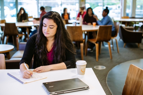 Student taking notes in university library cafe