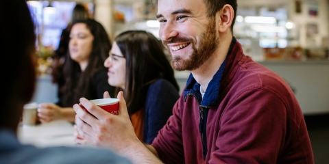 Students sat around a table smiling and talking in the Library Café